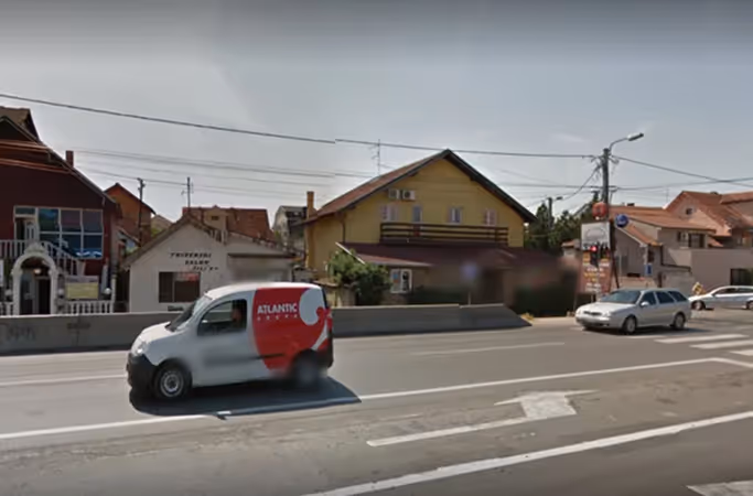 Ulični prizor Zrenjaninca s dostavnim vozilom i okolnim zgradama.